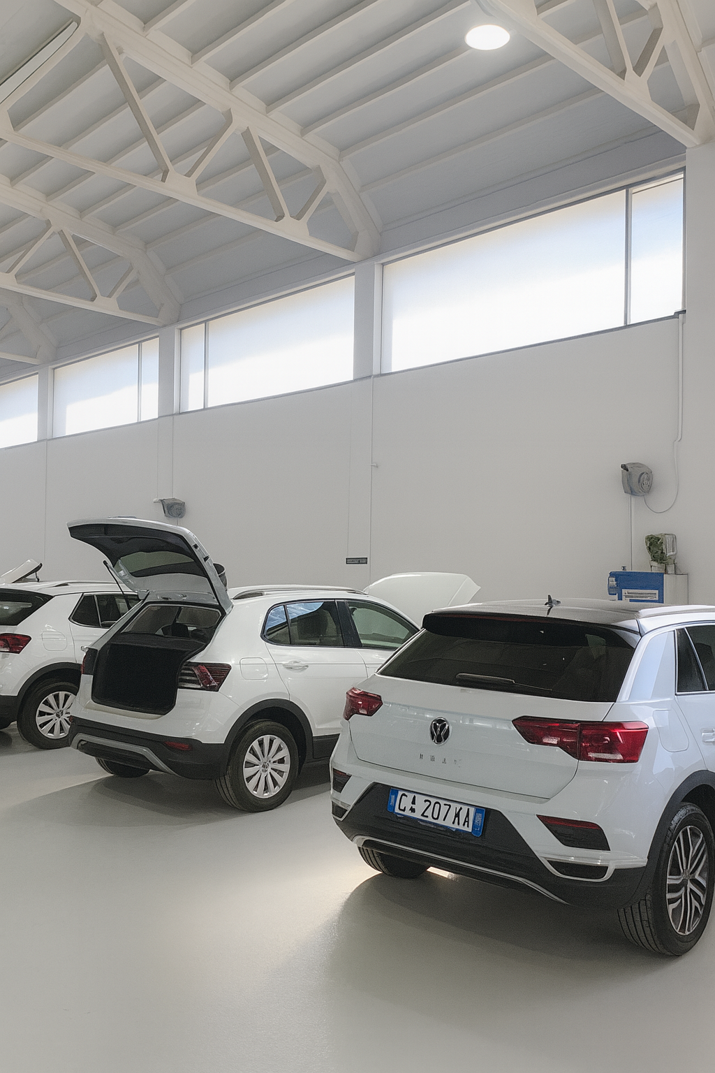 Capannone di carrozzeria con SUV bianchi in lavorazione, muri e vetri puliti e illuminazione uniforme.